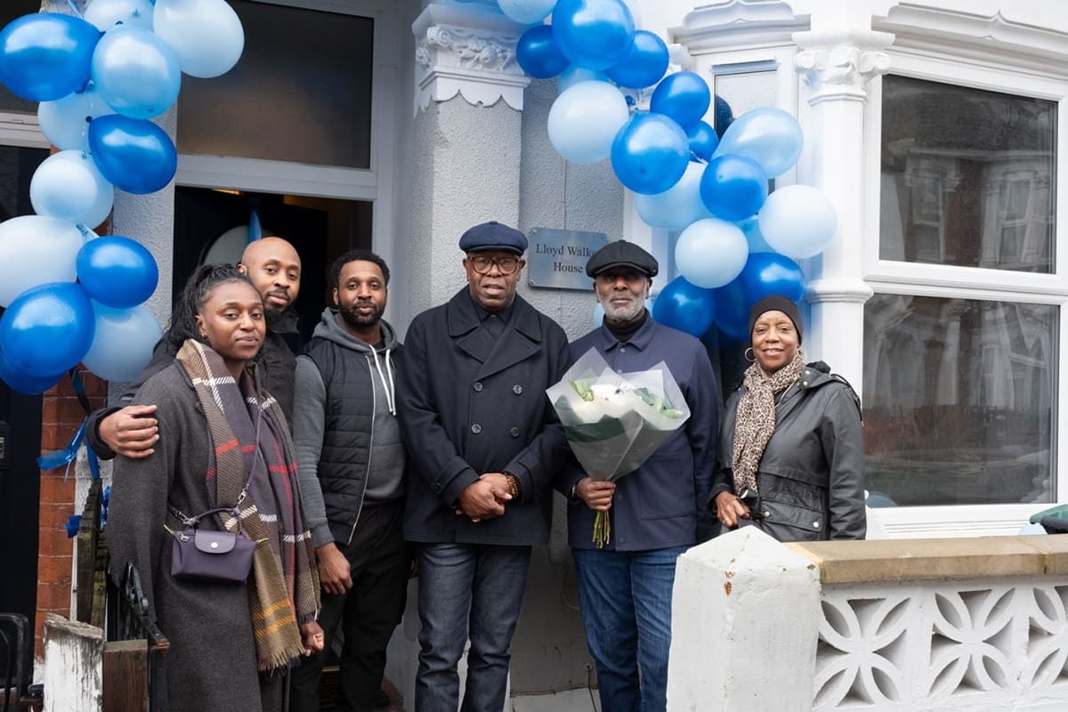 Six people standing outside a white building entrance with blue and white balloons