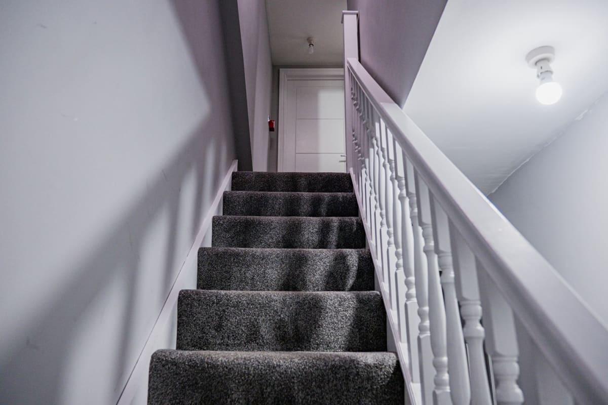 Staircase with dark gray carpet and white spindle railings, white walls and ceiling