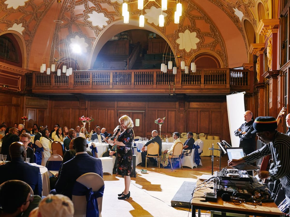 Speaker addresses seated guests at formal event in ornate historic hall with wood paneling