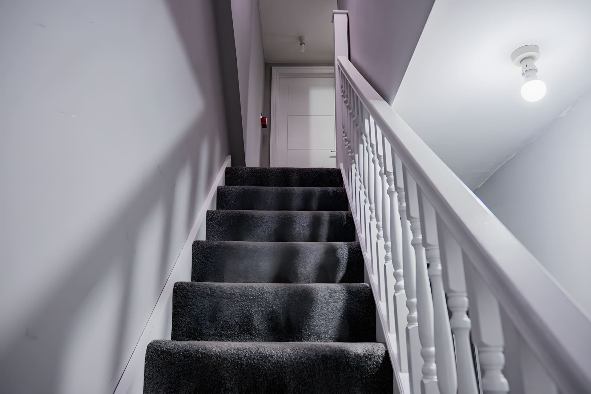 Staircase with black carpet and white railings leading upward in residential hallway