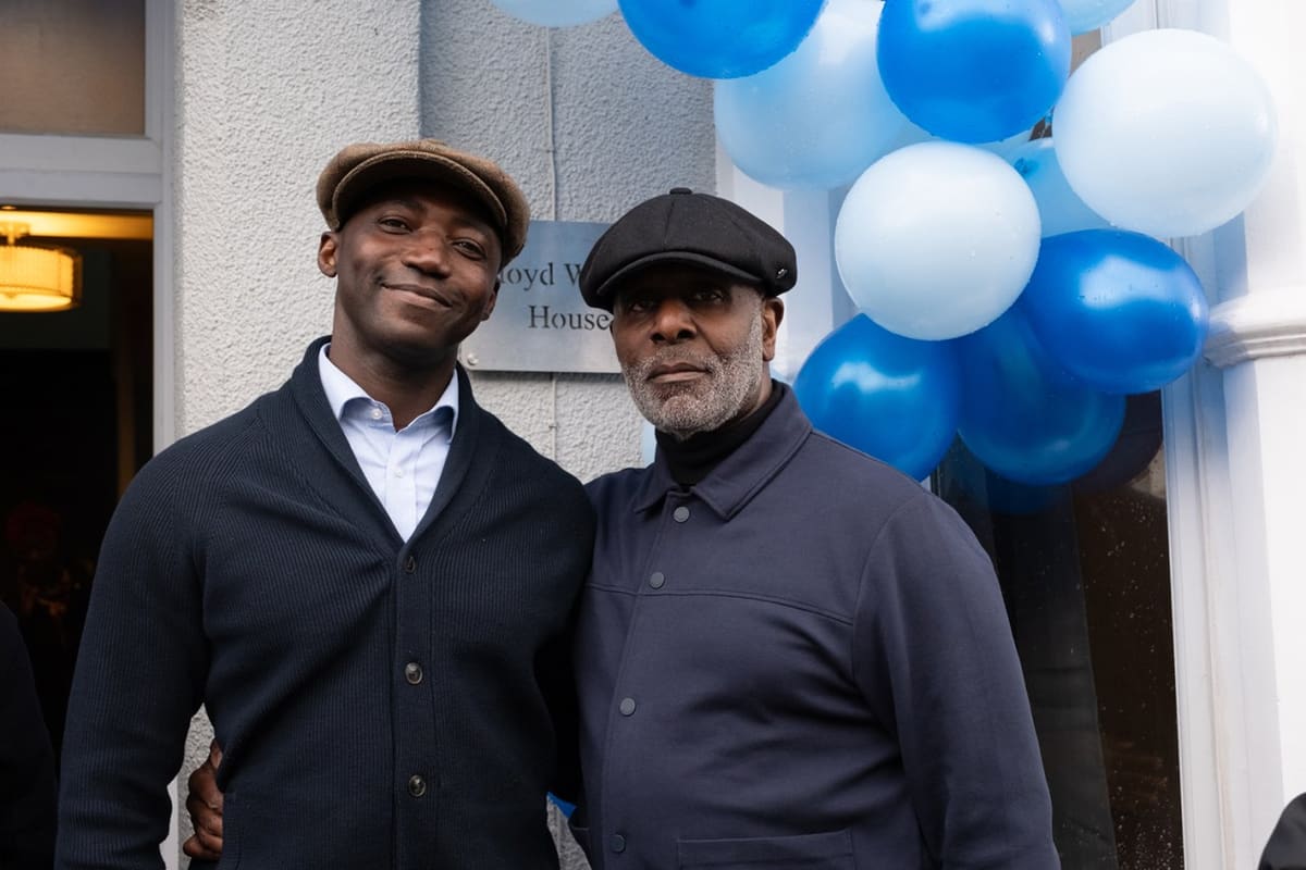 Two men smiling at entrance with blue and white balloons behind them