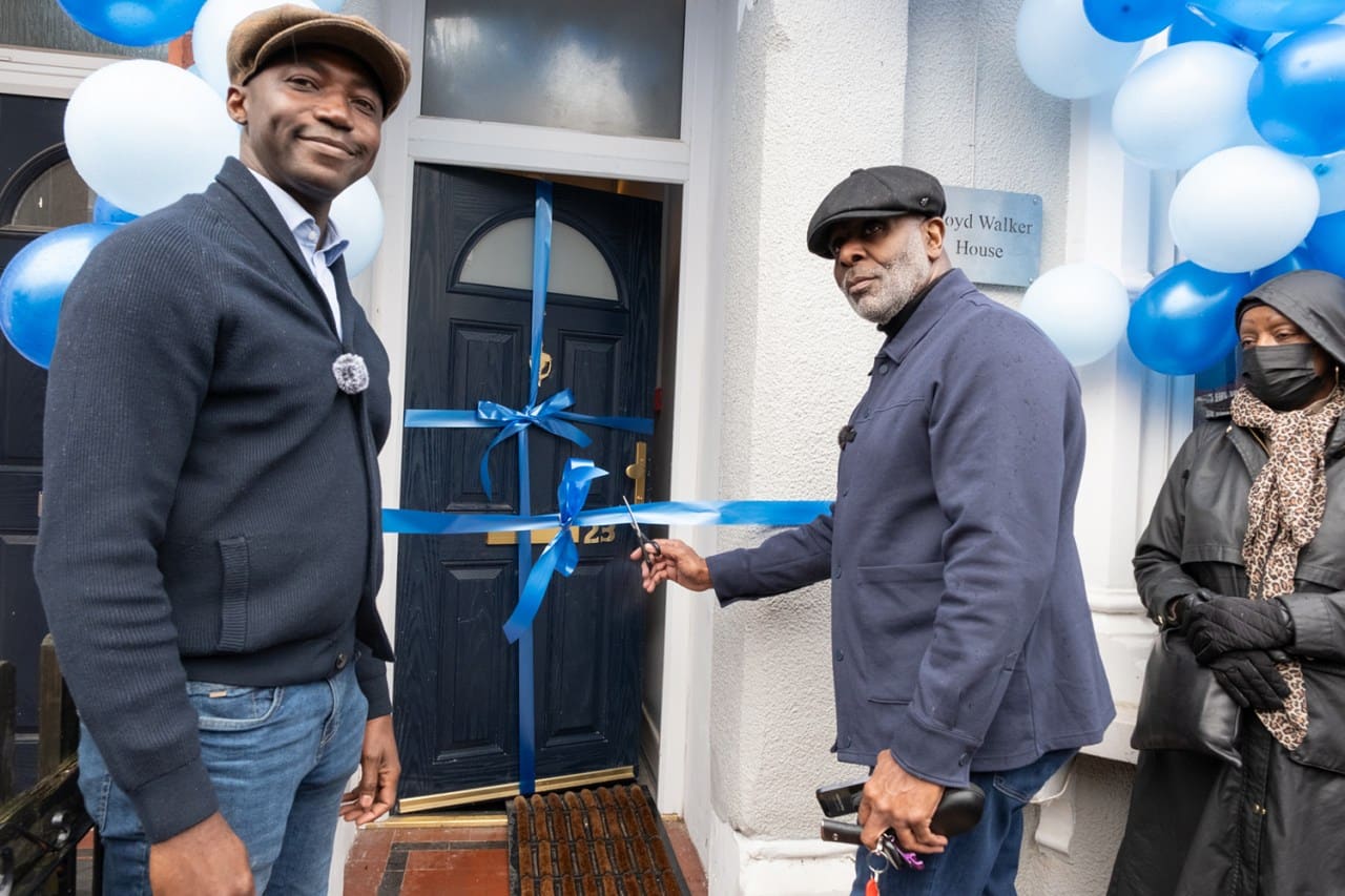 Man cutting blue ribbon at residential house entrance with blue and white balloons