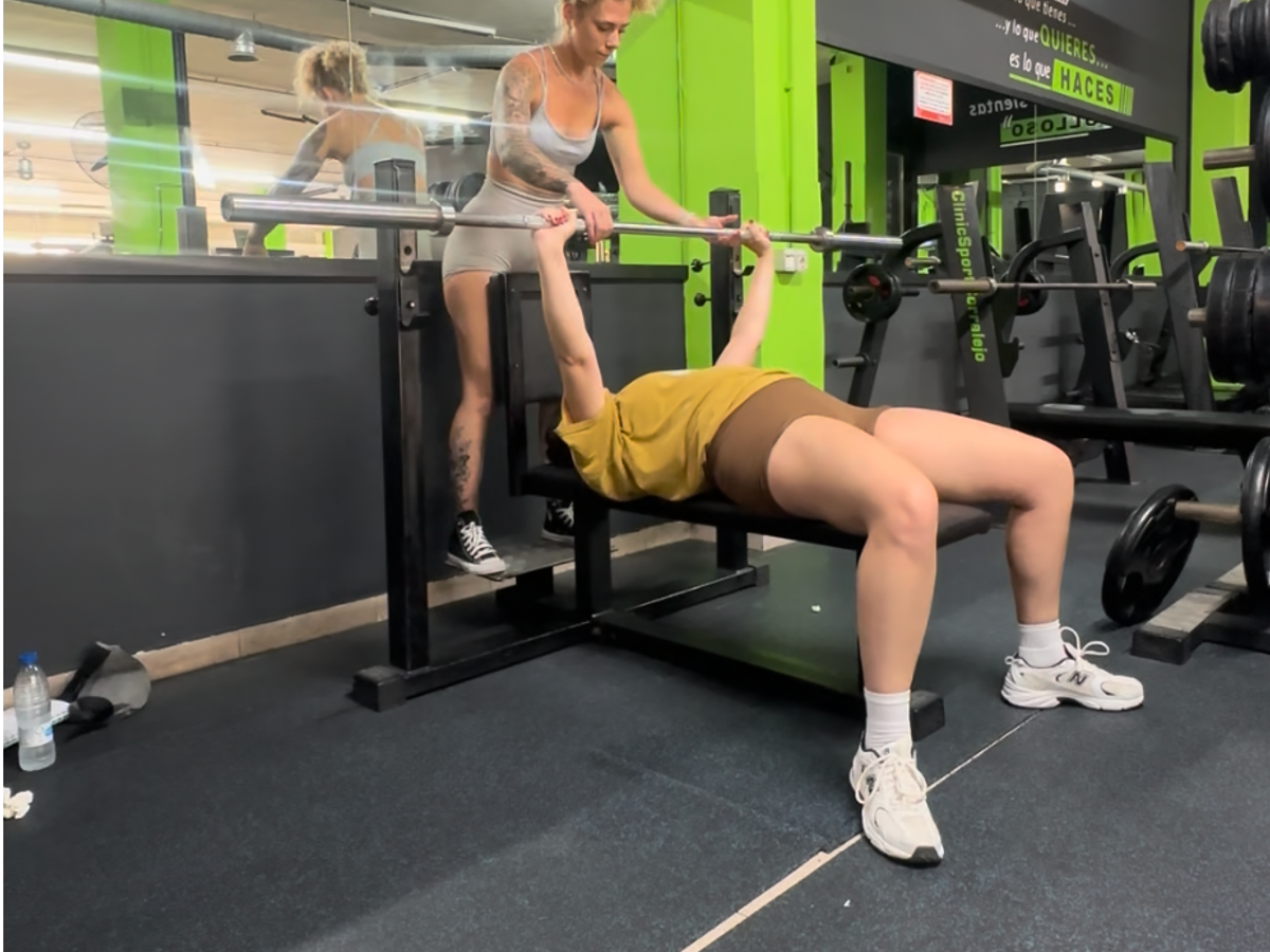 Personal trainer assisting client with barbell bench press in modern gym