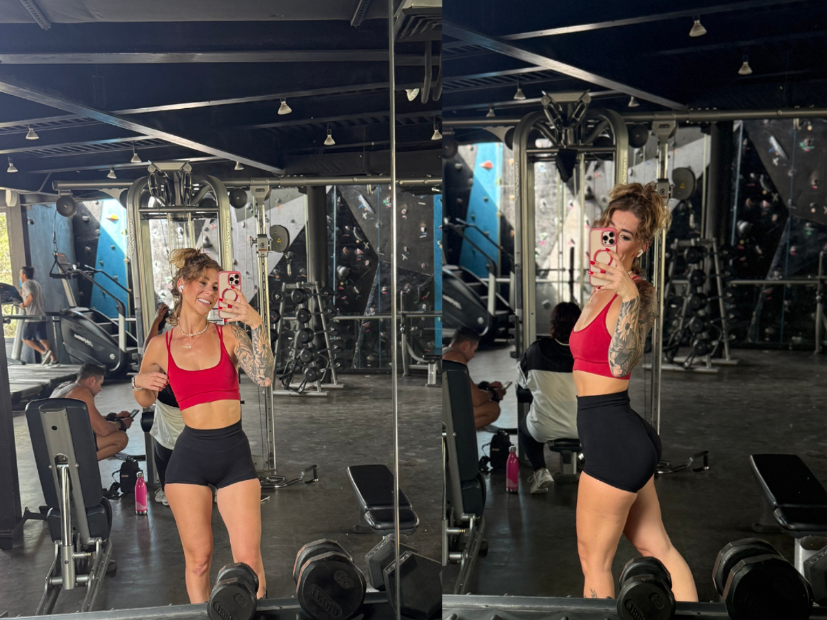 Woman in red sports bra and black shorts taking selfie in gym mirror with dumbbells