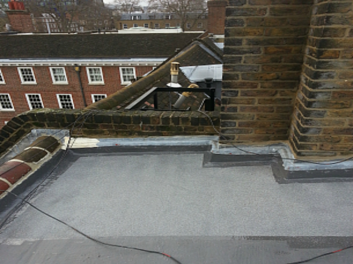 Flat roofing installation on urban building with brick chimney and parapet wall
