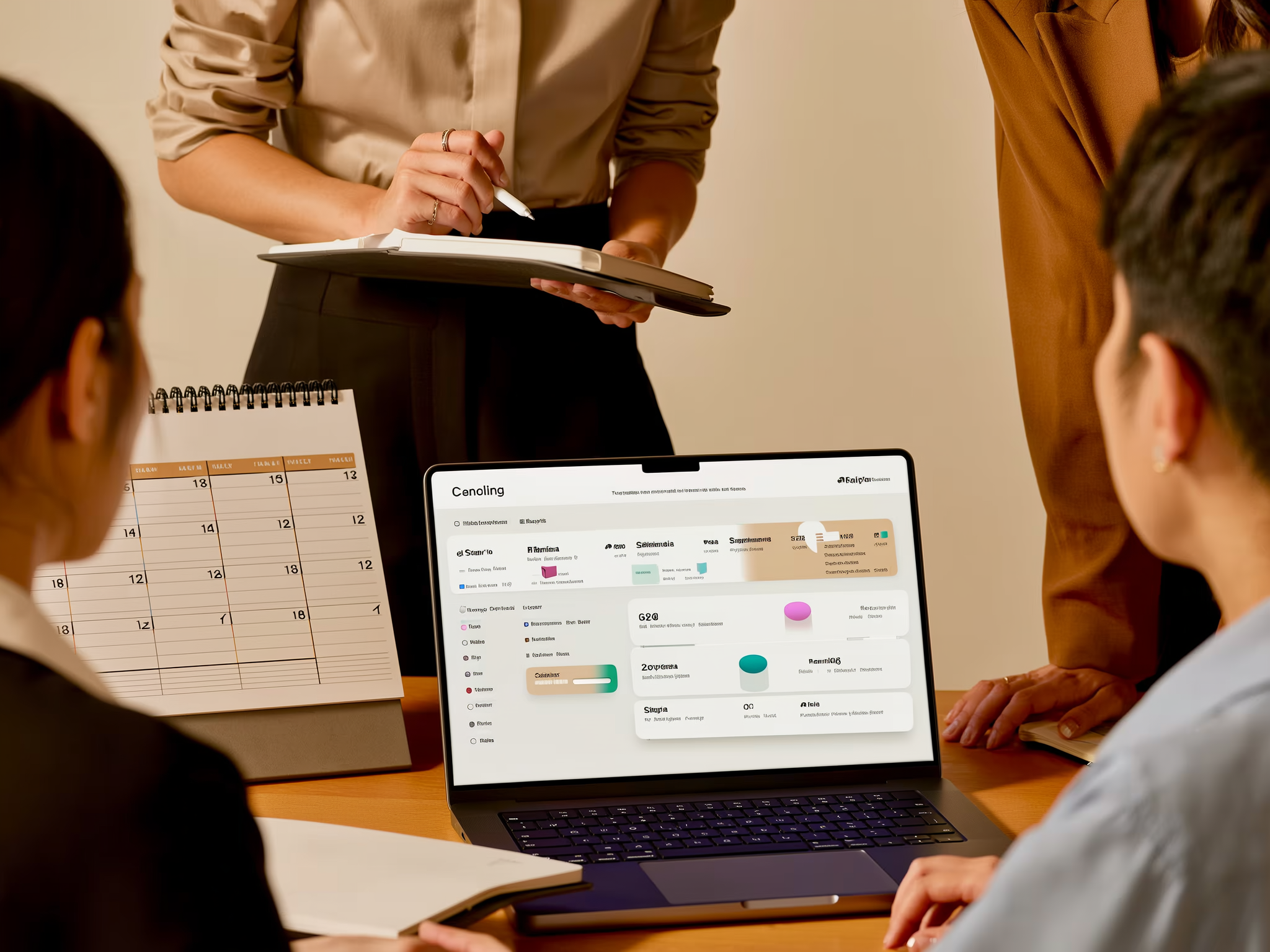Team members gathered around a laptop displaying a project management interface, with a calendar notebook visible