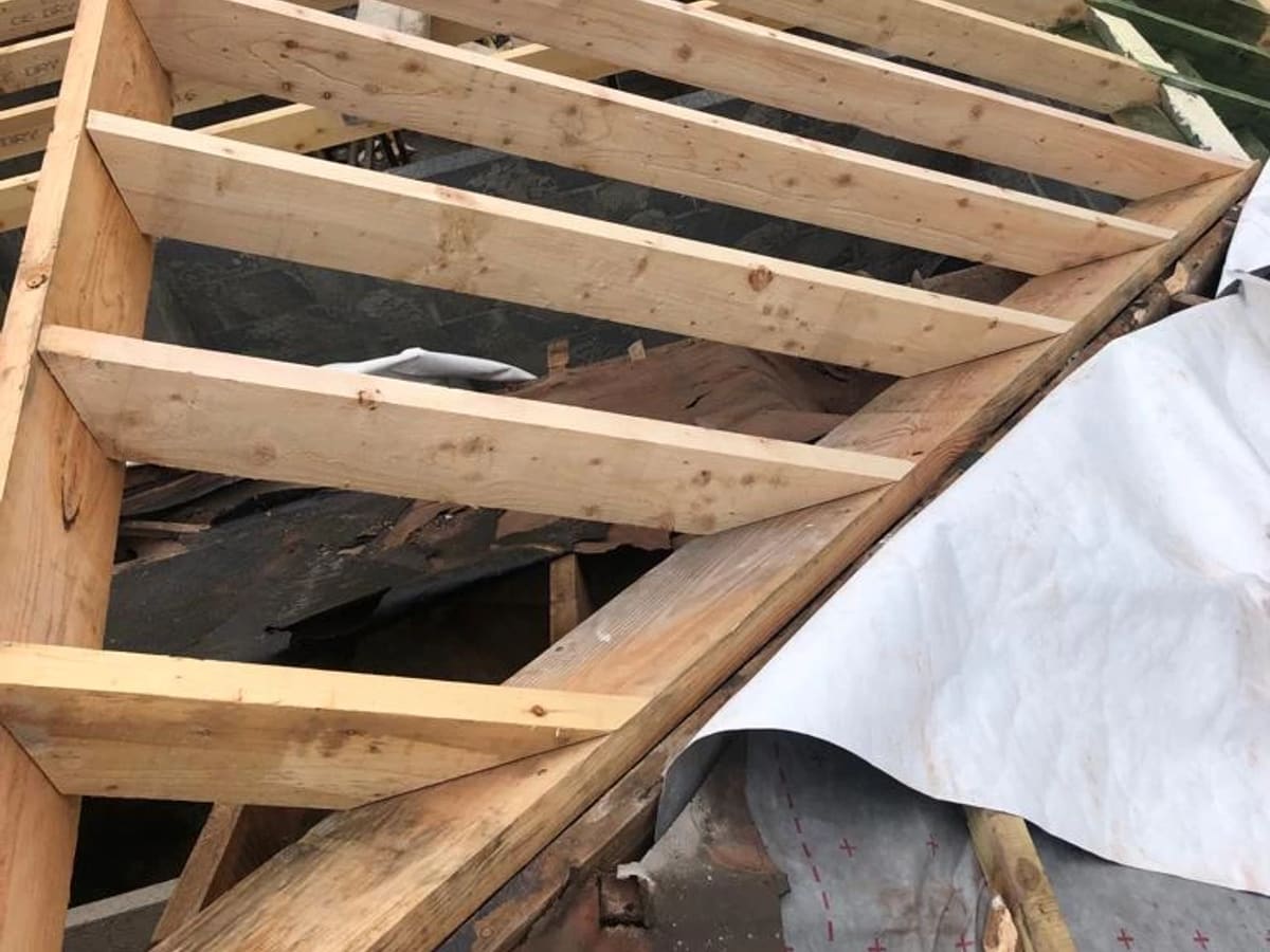 Wooden roof trusses and framing structure under construction, showing exposed beams and dark underlayment.