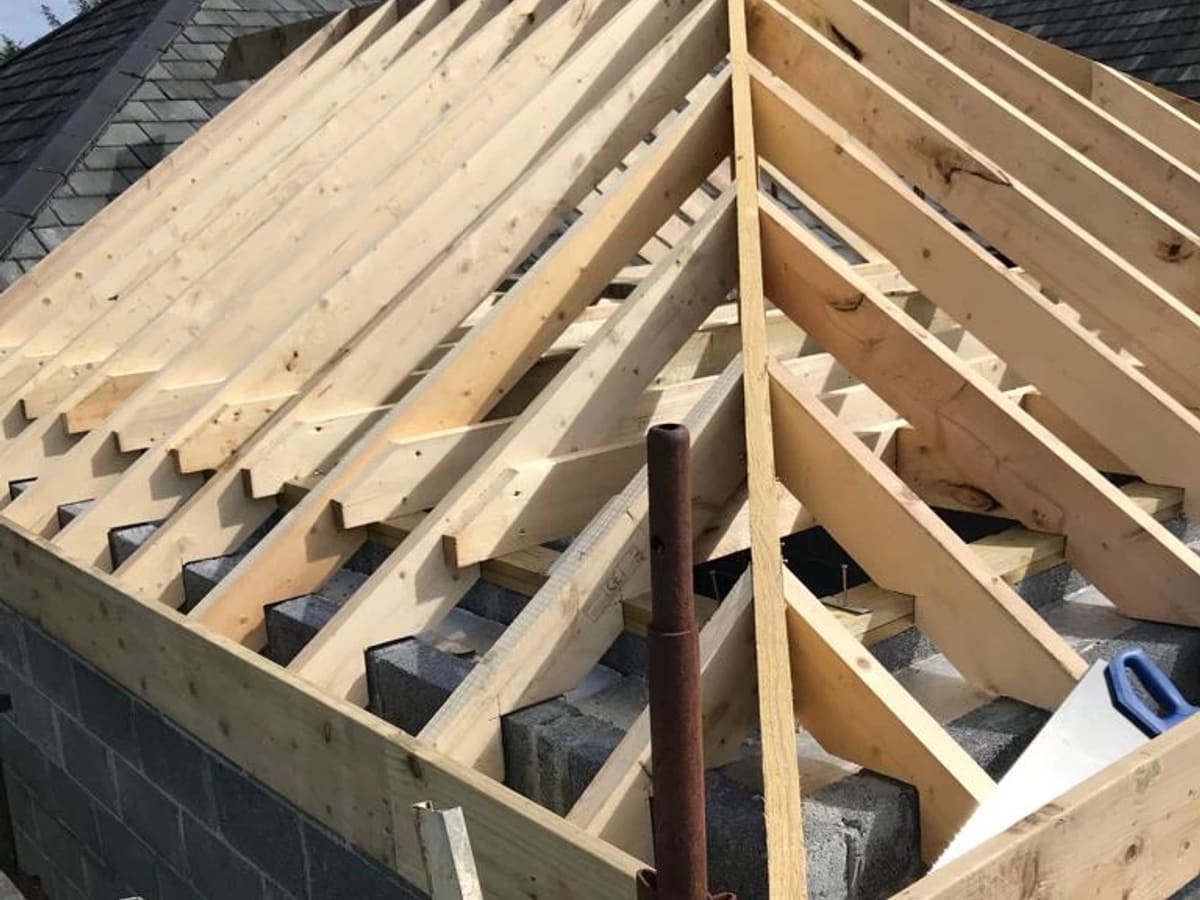 Wooden roof trusses and framing during construction, with brick wall below