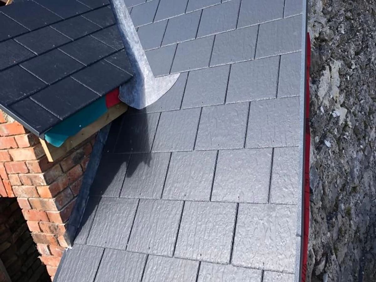 Gray slate roof tiles with white mortar joints and guttering visible