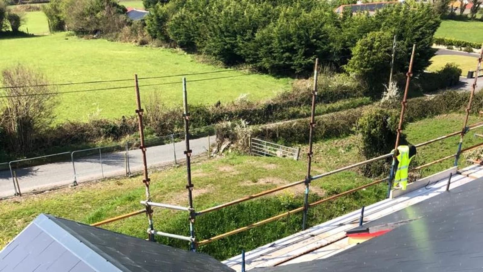 Roofer in safety vest installing metal railings on new roof with rural countryside view