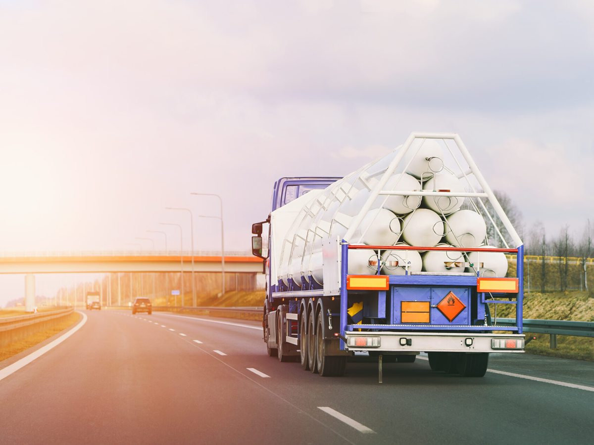 Large truck with white cylindrical cargo containers driving on highway at sunrise