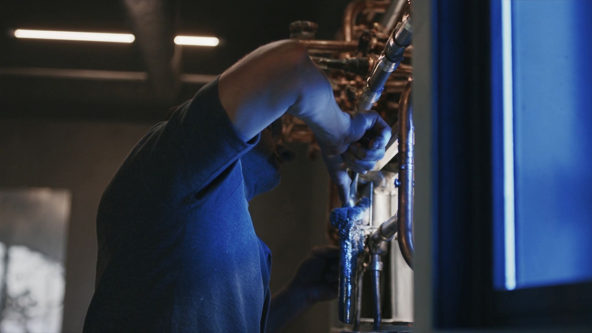 Worker in blue uniform installing or adjusting copper pipework in an industrial setting