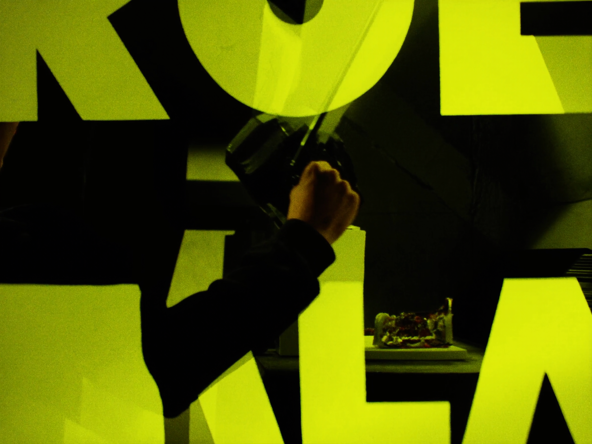 Person holding camera photographing small object surrounded by large yellow letters