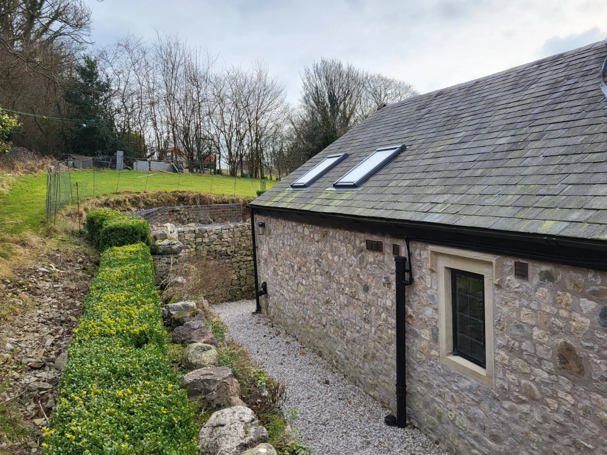 Stone cottage with slate roof, skylights, gravel path, ivy-covered stone wall, rural hillside setting