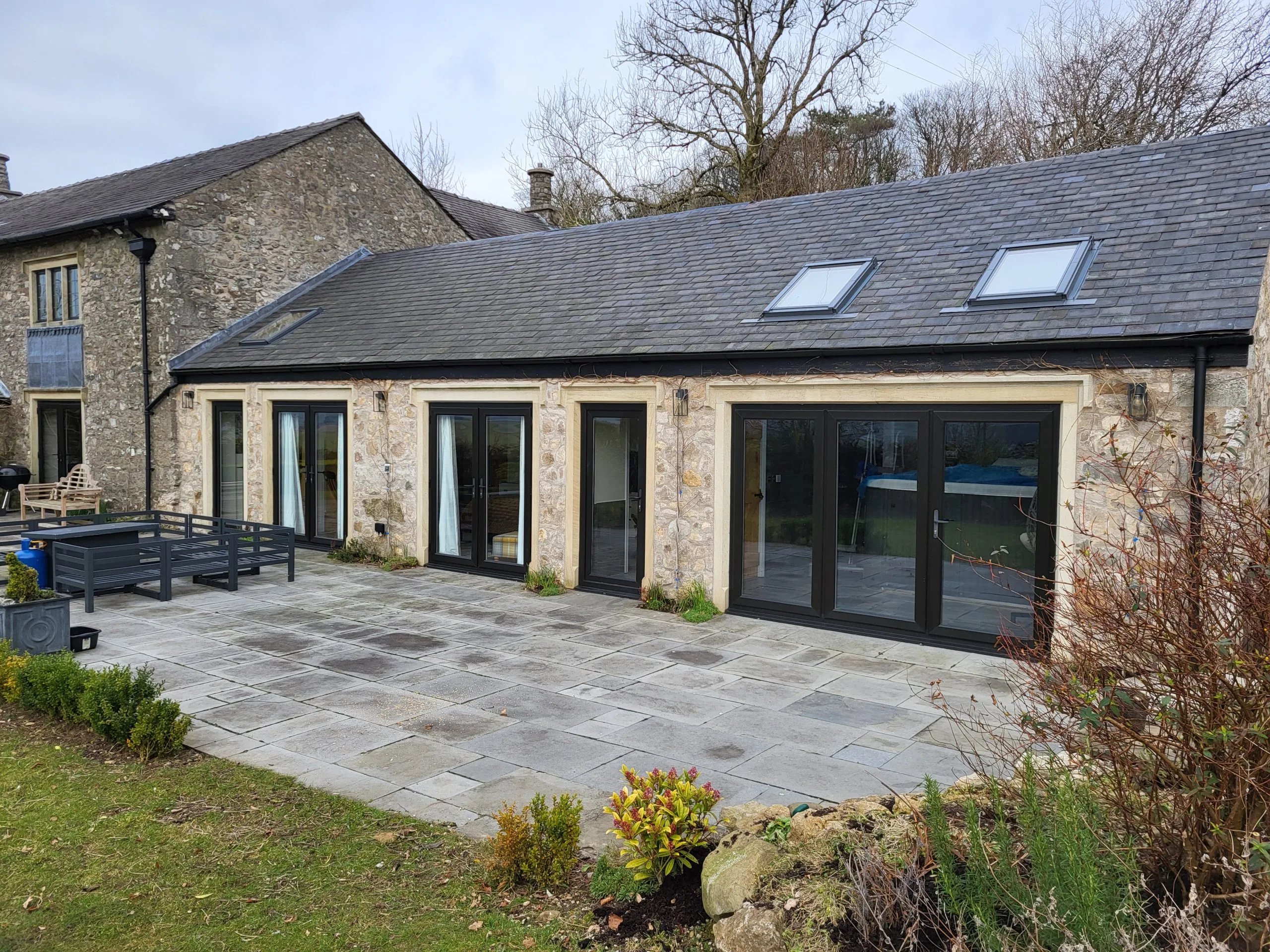 Stone cottage with slate roof, black-framed doors and windows, new patio area