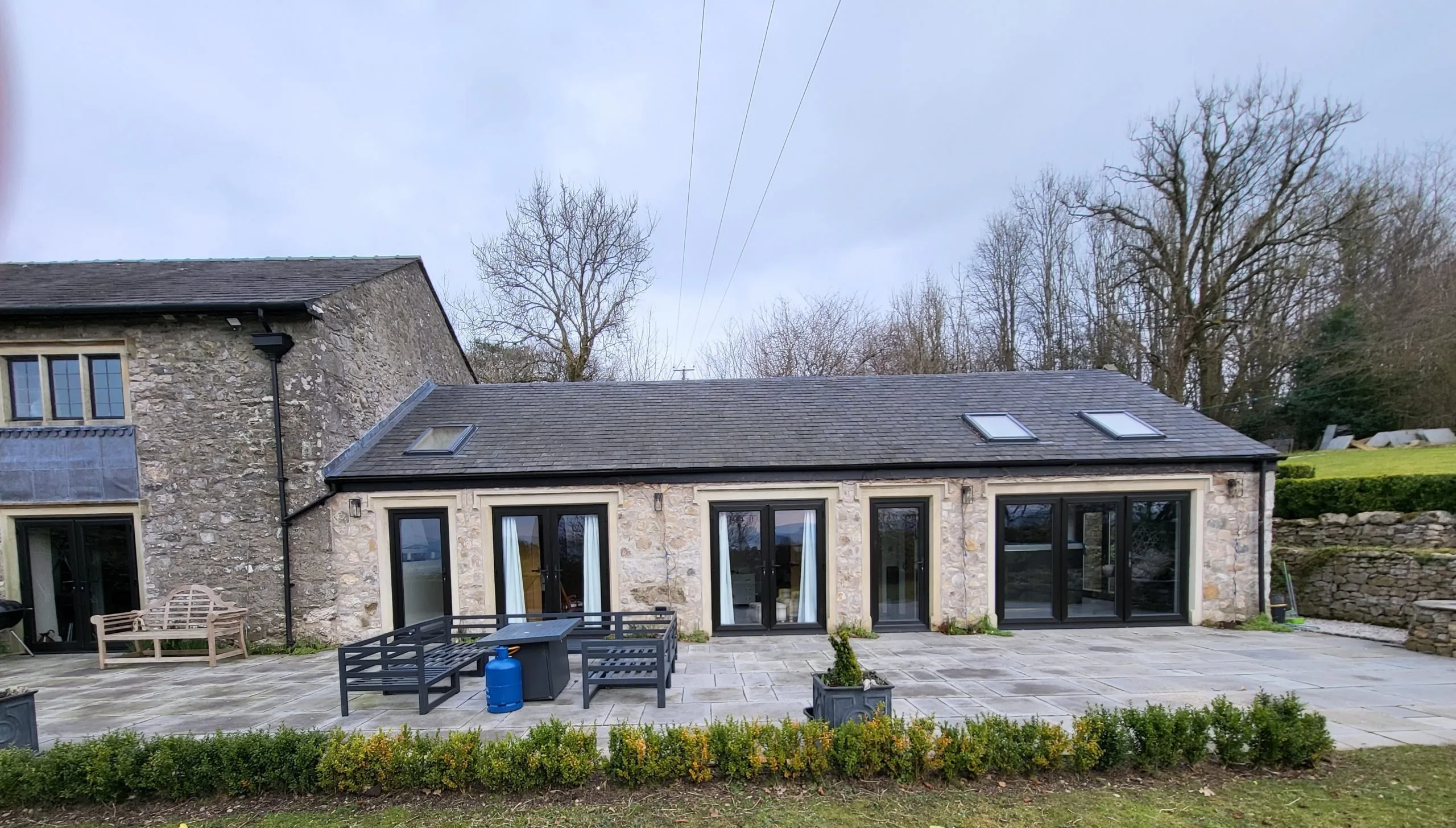 Stone extension with slate roof, large black-framed windows and glass doors, patio area
