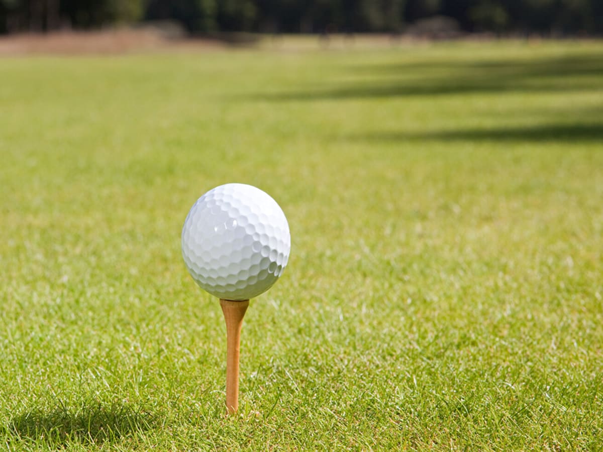 White golf ball on wooden tee on green grass fairway