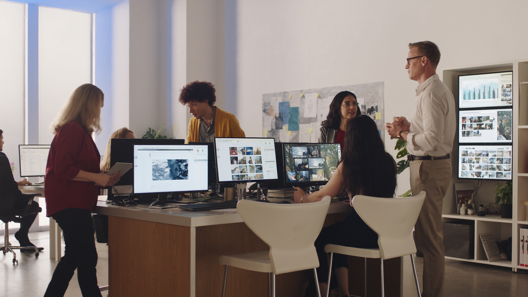 Small team reviewing photos and designs on computer monitors in bright office