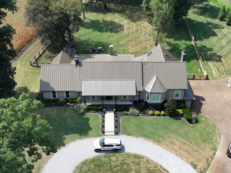Aerial view of residential home with metal standing seam roof and manicured grounds