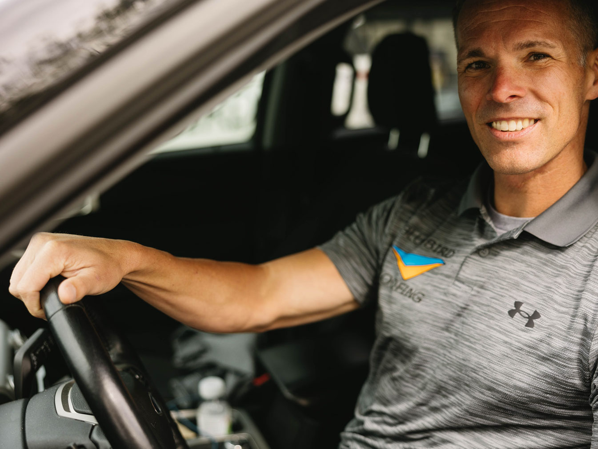 Smiling man in work polo shirt sitting in driver's seat of vehicle