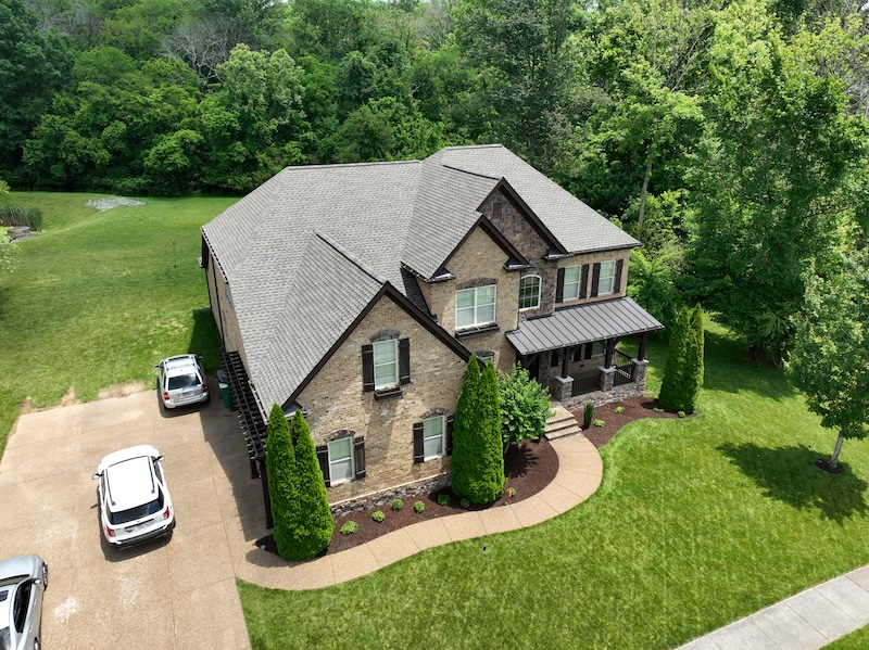 Aerial view of two-story brick residential home with gray roof and manicured landscaping