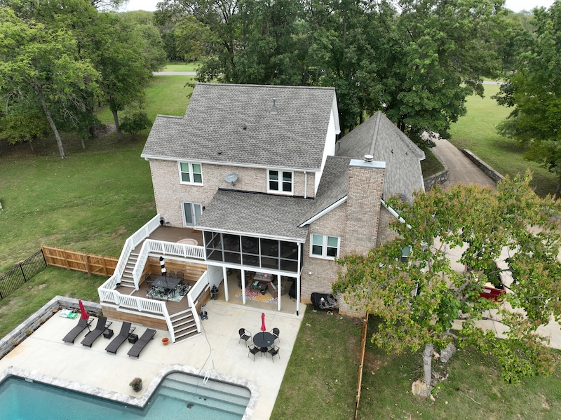 Aerial view of two-story brick home with deck, screened porch, pool, and landscaped yard