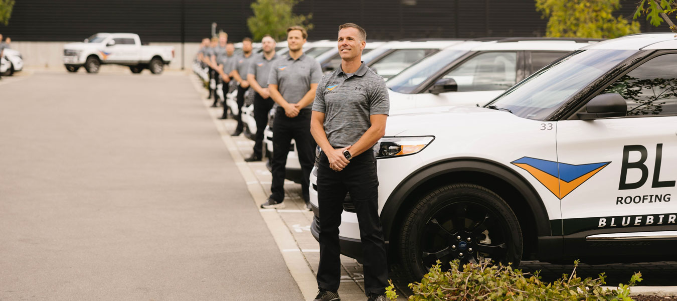 Roofing company team standing in line next to branded service vehicles in parking lot