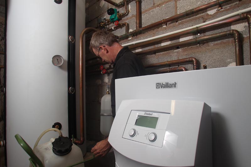Heating engineer inspecting copper pipes and Vaillant boiler system in utility room