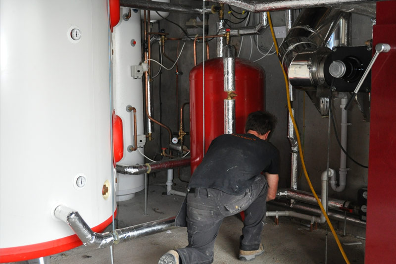 Technician working on red heating boiler and copper pipework in plant room