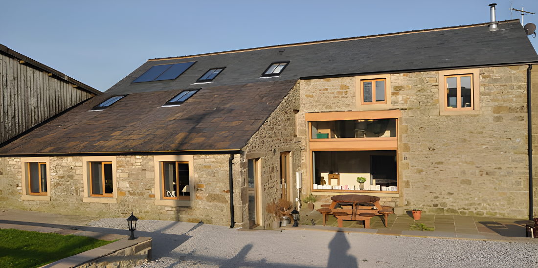 Stone barn conversion with modern wood-framed windows, solar panels, and outdoor seating area