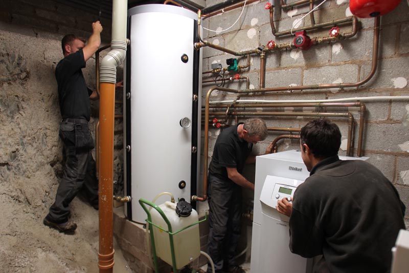 Three HVAC technicians working on water heater and copper piping in basement