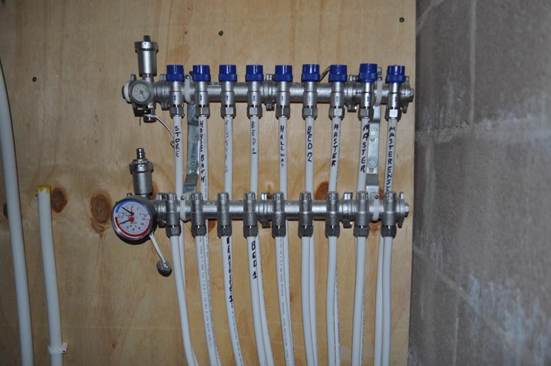 Radiant floor heating manifold with blue valve handles and pressure gauges mounted on wall