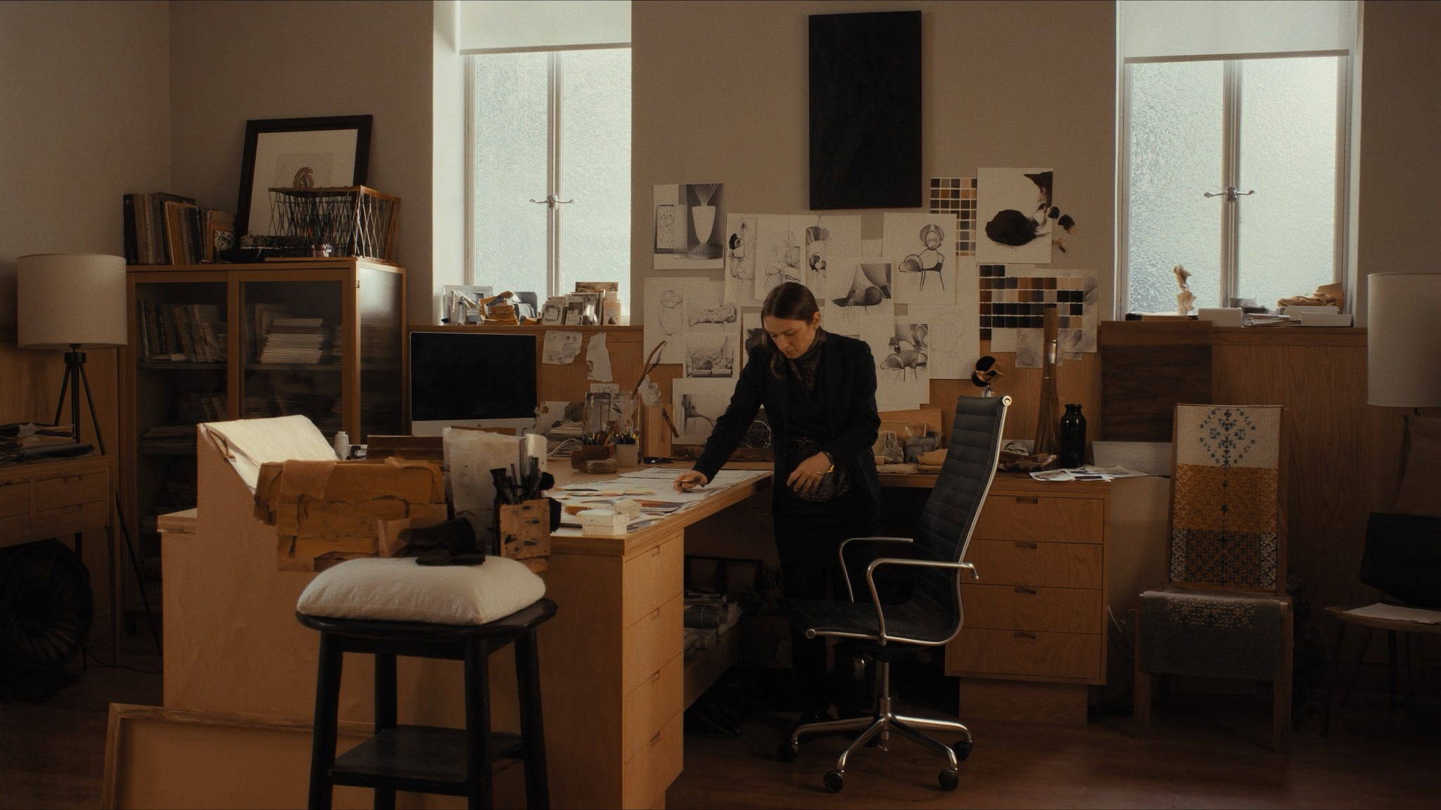 Designer working at cardboard desk in studio surrounded by sketches and wooden furniture