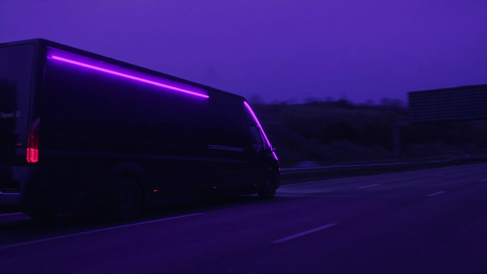 Dark delivery van with purple neon lighting on highway at dusk