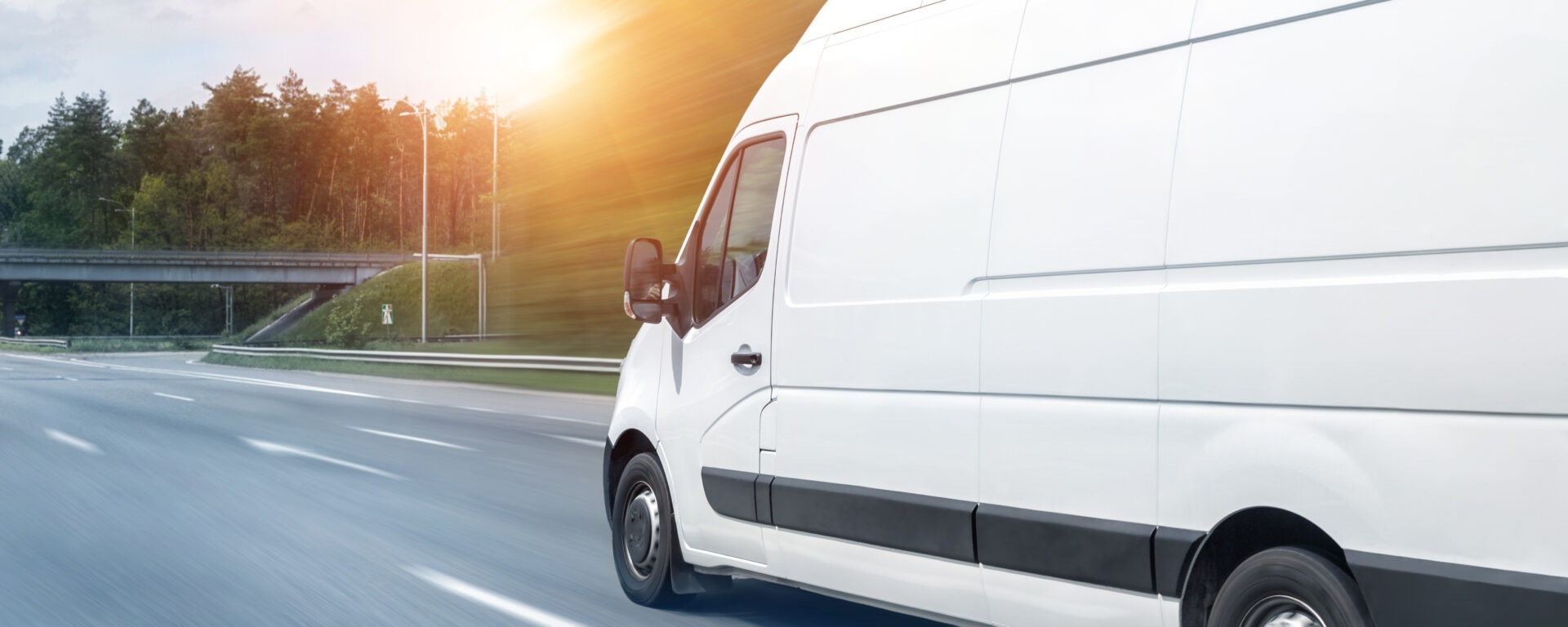 White delivery van driving on highway with forest and sunset in background