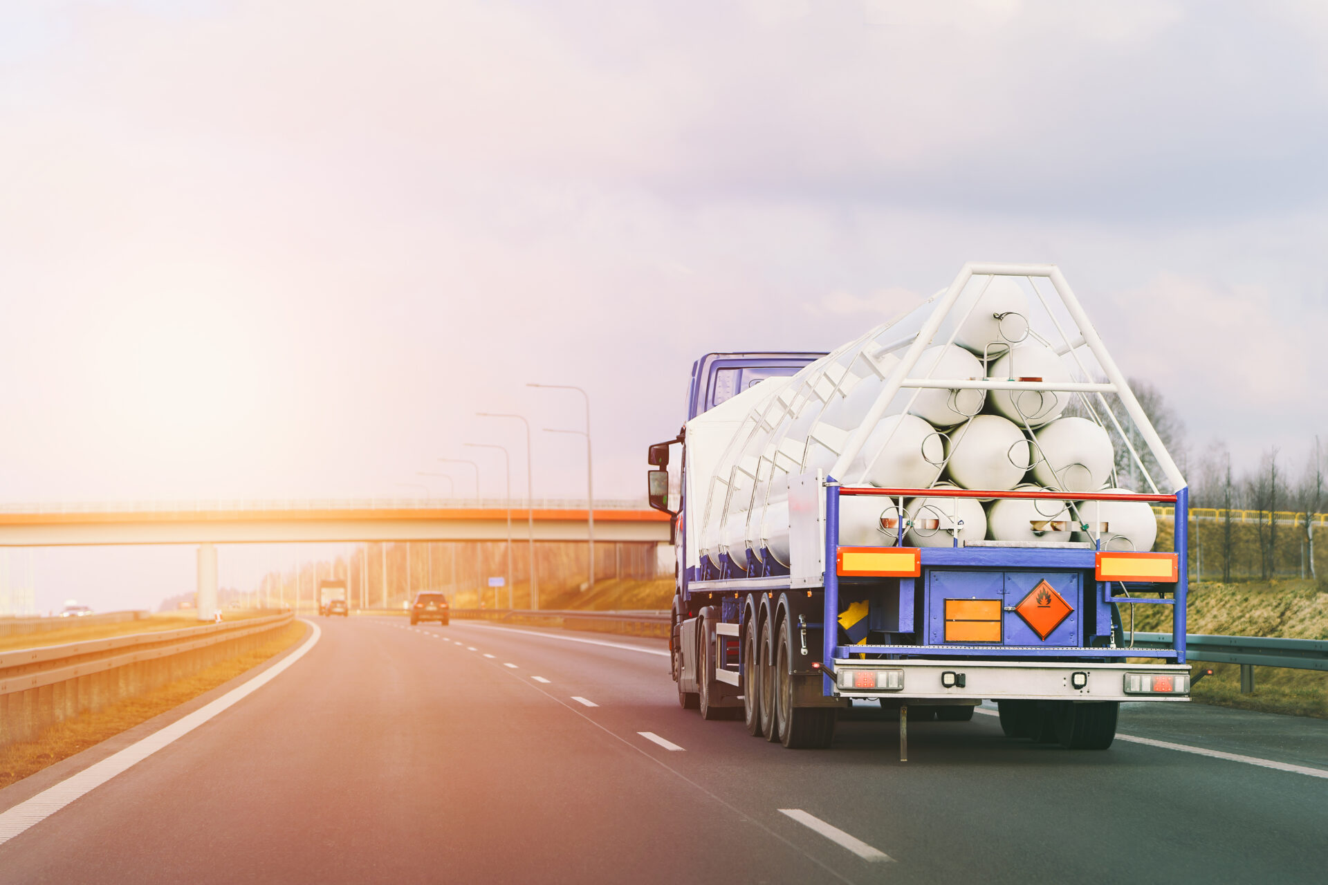 Truck carrying rolls of white material on motorway at sunrise with bridge ahead