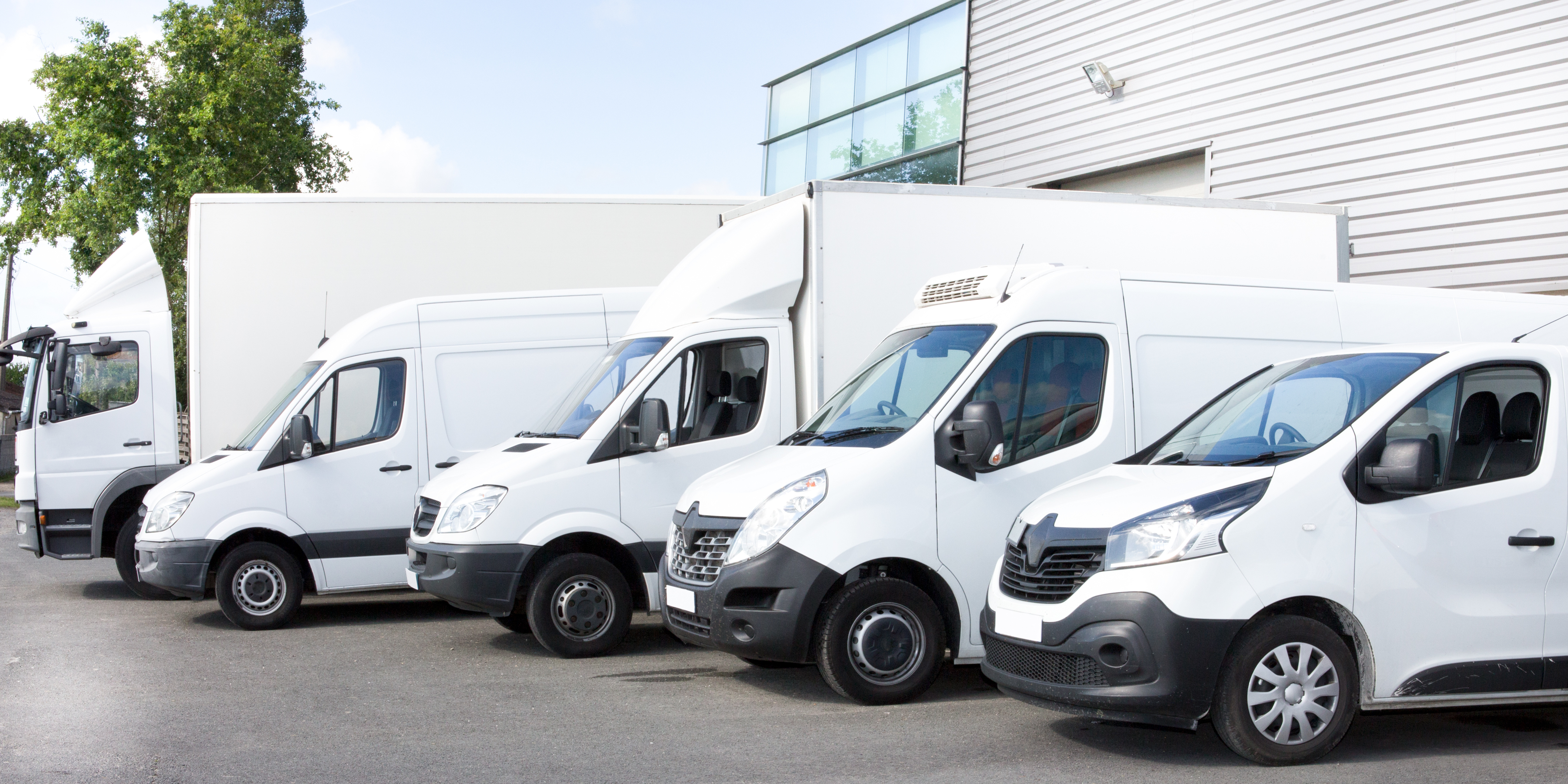 Row of white commercial vans parked outside an industrial building