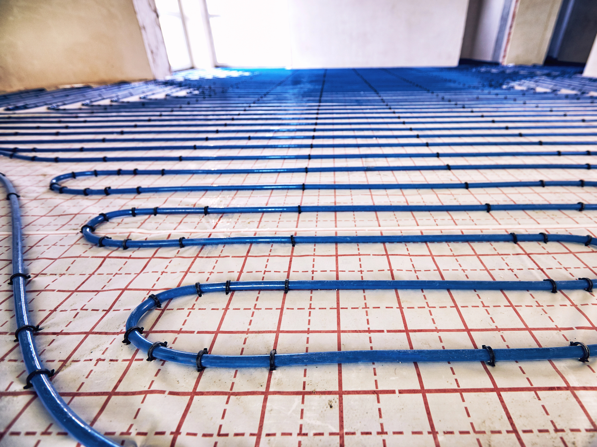 Blue radiant heating pipes laid in parallel loops on floor with red grid markings beneath