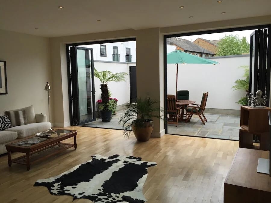 Bright living room with black-framed glass doors opening onto a paved garden patio with seating
