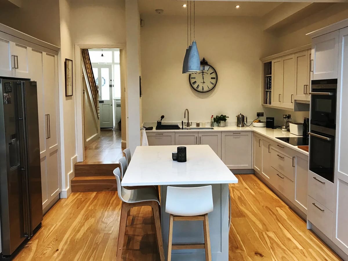 Modern kitchen with cream cabinets, white island, wooden flooring, and blue pendant light