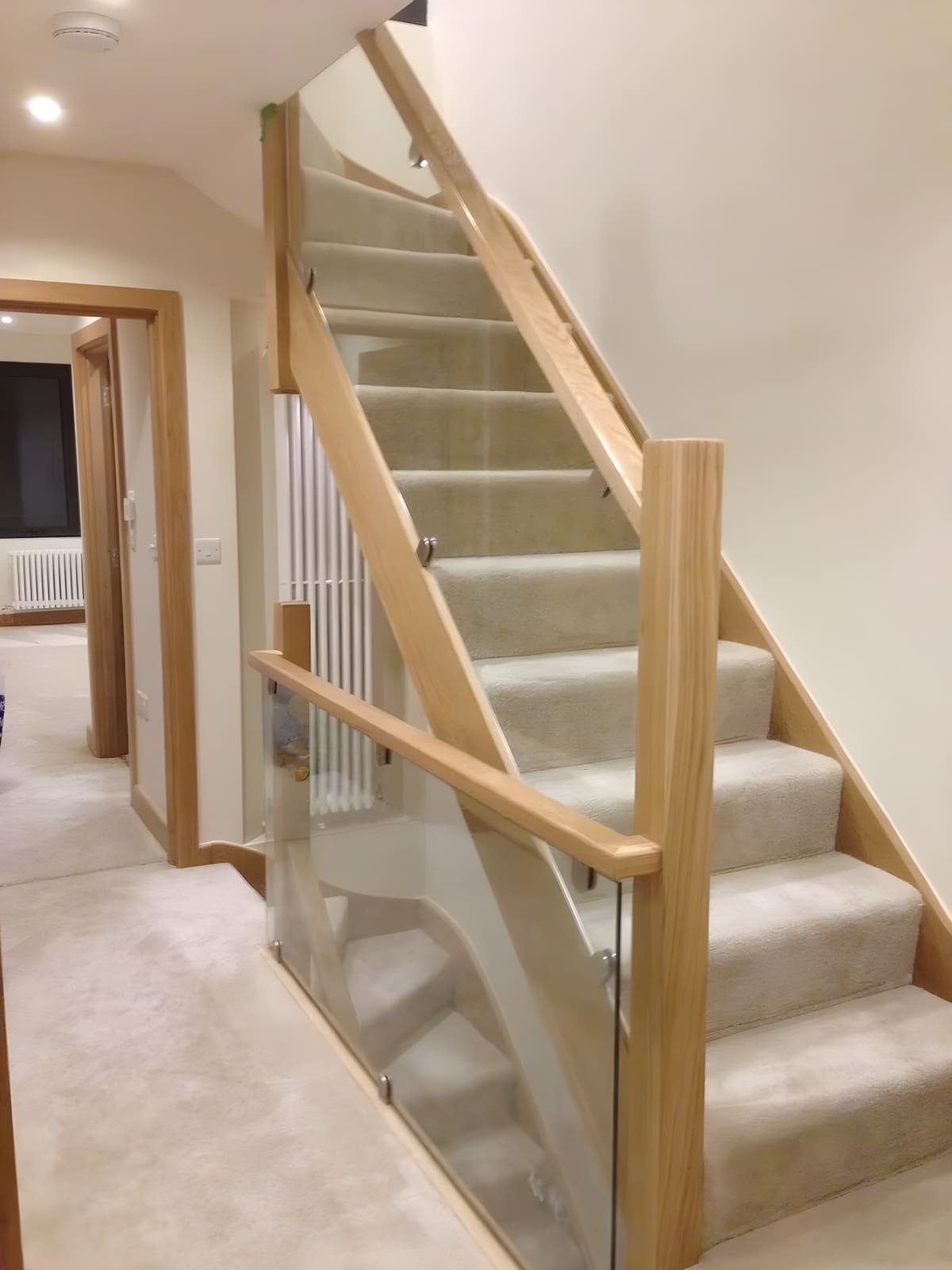 Modern staircase with wooden handrails and glass balustrade in bright hallway