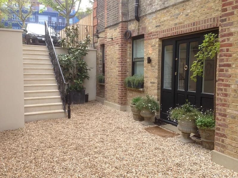 Brick courtyard with gravel surface, black doors, potted plants, and stairs