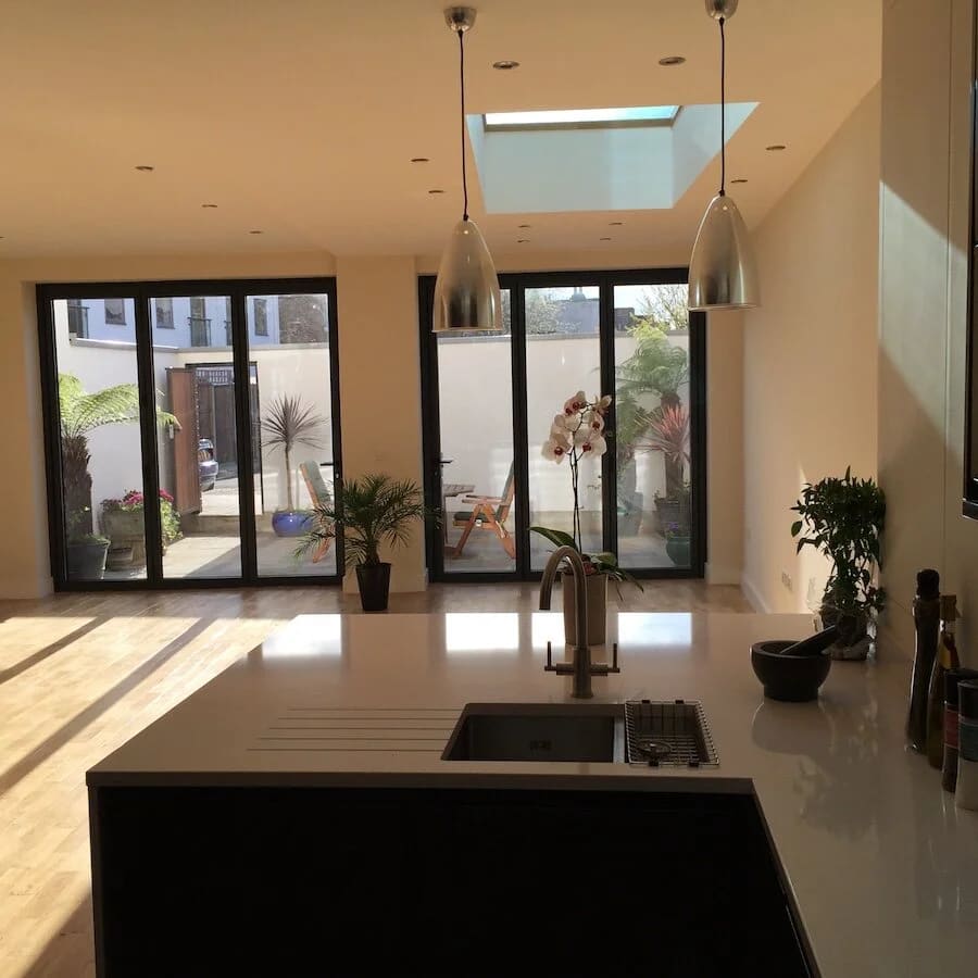 Modern kitchen with skylight, black island, pendant lights, and glass doors to courtyard